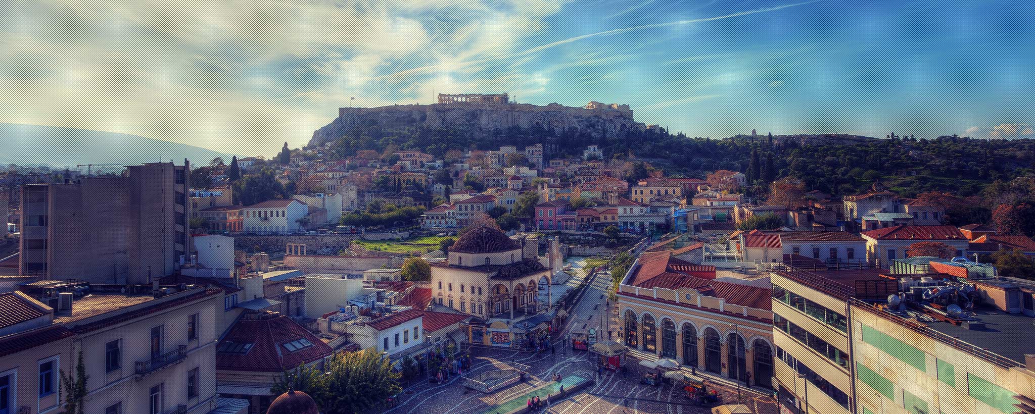 Elevated view of a hillside old town with a hilltop citadel and ruins in the background, colorful rooftops and a domed building under warm Mediterranean light