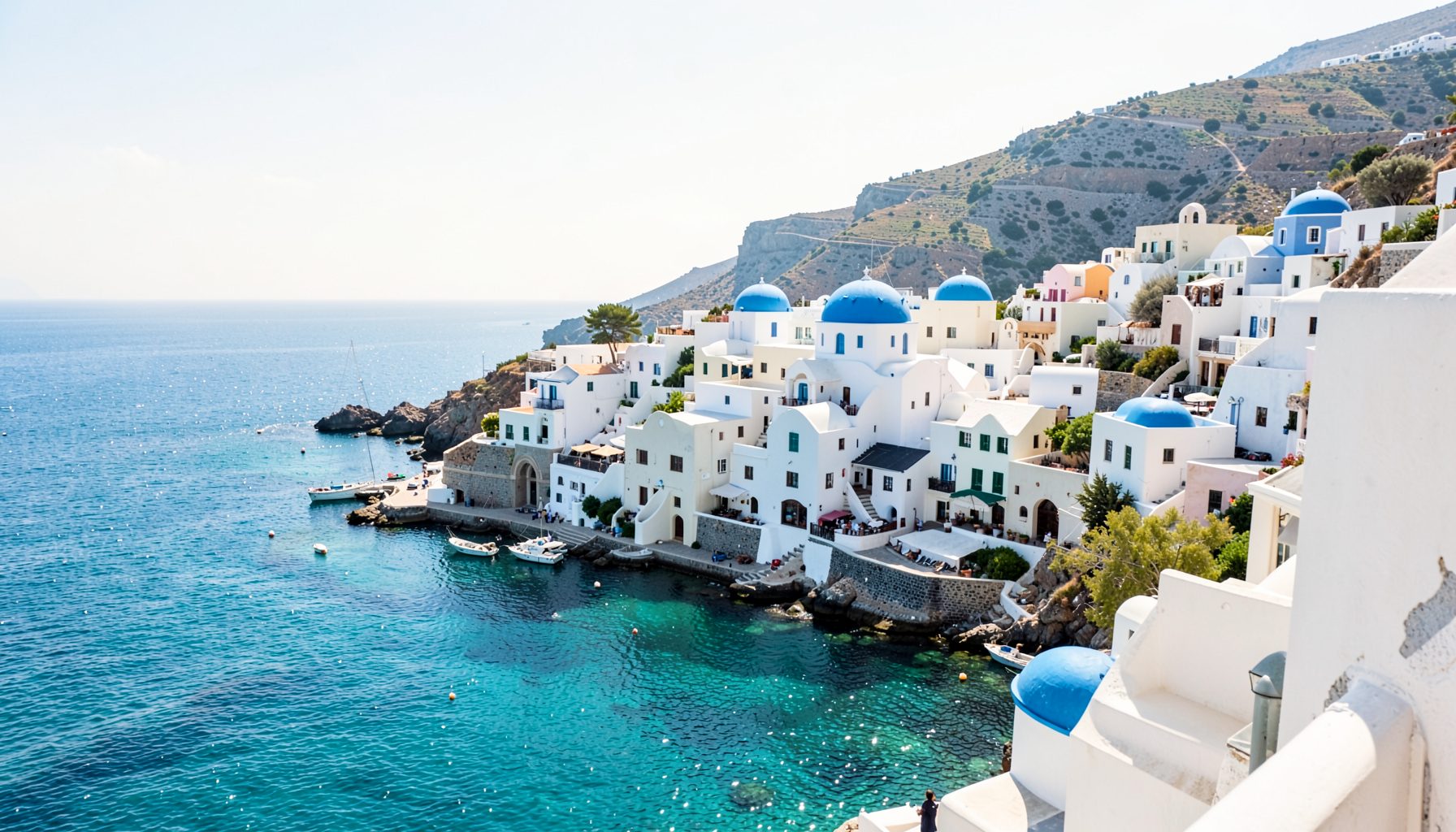 Sunlit whitewashed coastal village with blue-domed buildings overlooking a sparkling turquoise sea
